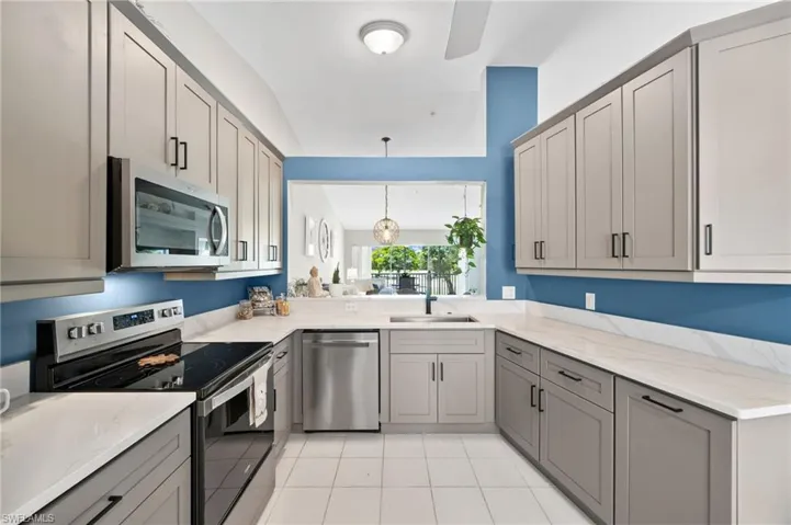 Kitchen featuring light stone countertops, light tile floors, hanging light fixtures, gray cabinetry, and appliances with stainless steel finishes