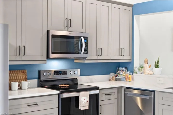 Kitchen with gray cabinets, light stone countertops, and stainless steel appliances