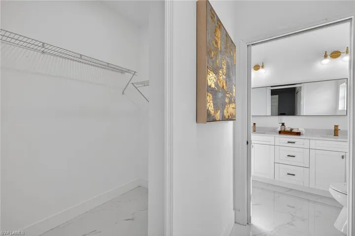 Full bath featuring light marble finish flooring, a walk in closet, and double vanity