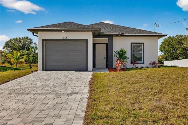 View of front of home with stucco siding, a front lawn, decorative driveway, a garage, and roof with shingles