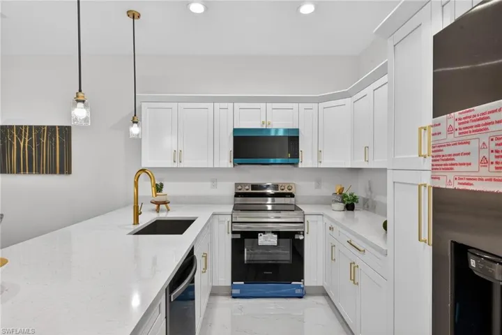 Kitchen featuring fridge with ice dispenser, stainless steel range with electric stovetop, decorative light fixtures, light stone countertops, and white cabinetry