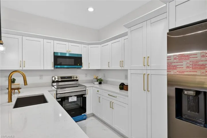 Kitchen with stainless steel appliances, white cabinets, light marble finish flooring, light stone countertops, and recessed lighting