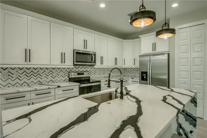 Kitchen with pendant lighting, stainless steel appliances, white cabinetry, light stone countertops, and decorative backsplash