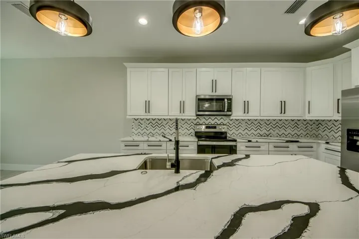 Kitchen featuring light stone counters, decorative backsplash, stainless steel appliances, and white cabinets