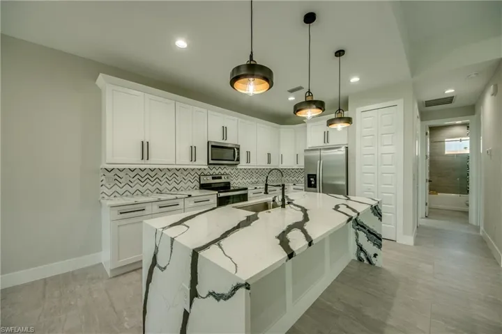 Kitchen featuring white cabinets, light stone countertops, a center island with sink, decorative light fixtures, and stainless steel appliances