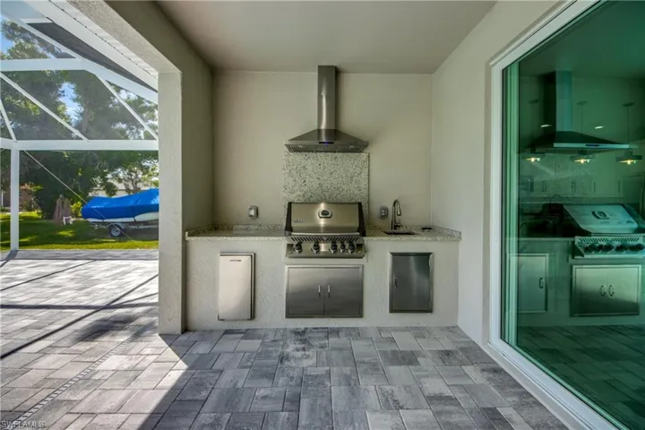 View of patio with glass enclosure, sink, an outdoor kitchen, and grilling area
