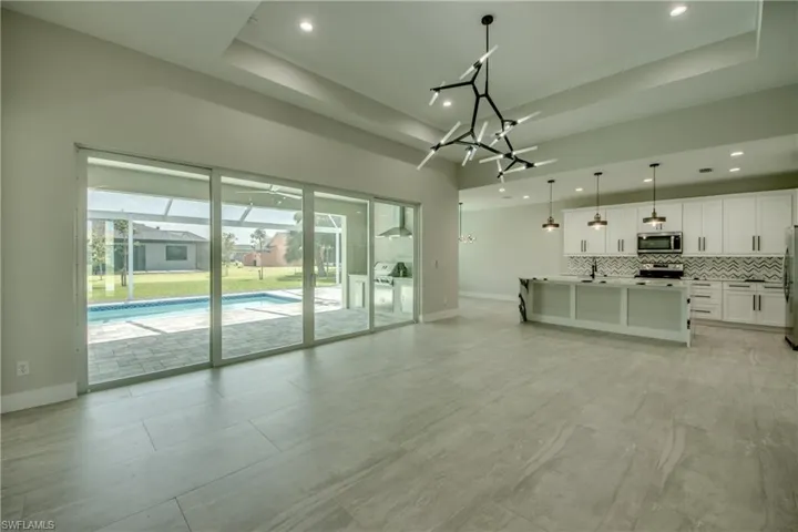 Unfurnished living room featuring light tile patterned flooring, sink, a tray ceiling, and an inviting chandelier
