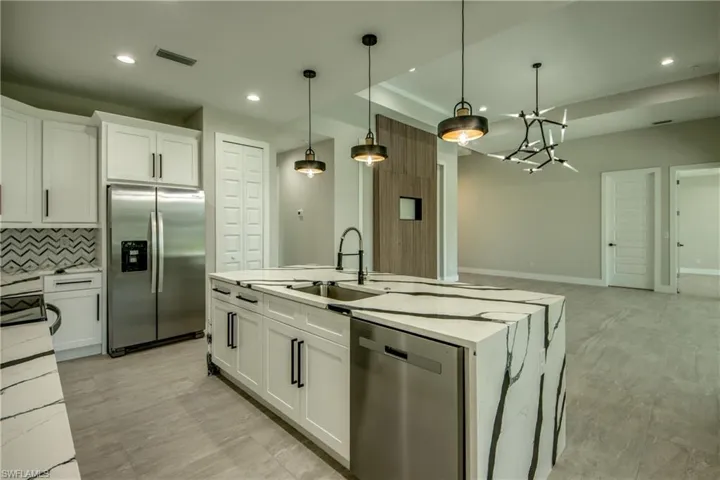 Kitchen with stainless steel appliances, decorative backsplash, light stone countertops, sink, and white cabinetry