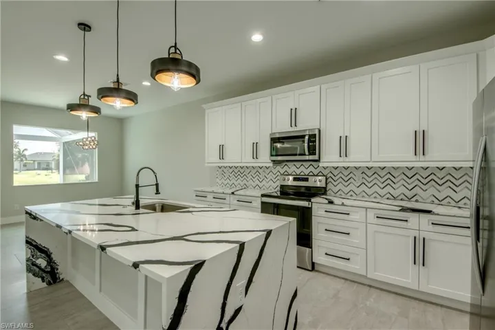 Kitchen featuring decorative backsplash, appliances with stainless steel finishes, white cabinets, a center island with sink, and decorative light fixtures