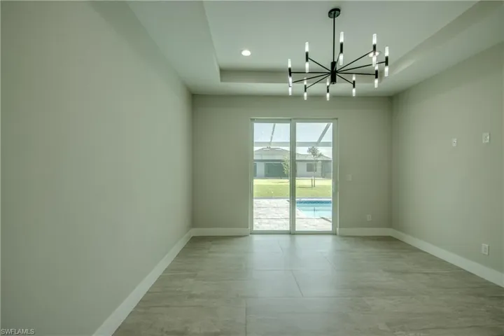 Spare room with a notable chandelier, a tray ceiling, and light tile patterned floors
