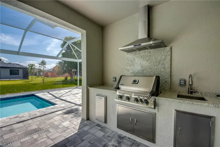 View of patio / terrace featuring glass enclosure, sink, exterior kitchen, and a grill