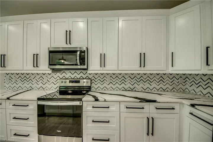 Kitchen with decorative backsplash, appliances with stainless steel finishes, white cabinets, and light stone countertops