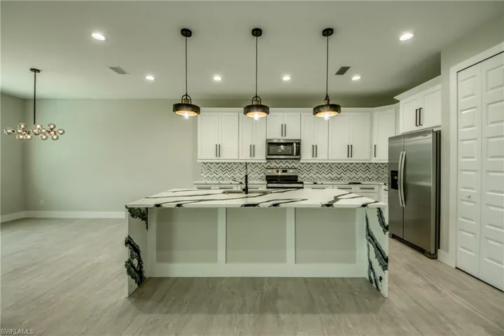 Kitchen with a center island with sink, white cabinets, stainless steel appliances, and decorative light fixtures