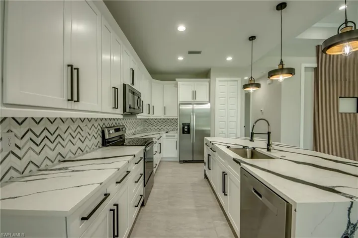 Kitchen with white cabinets, a center island with sink, decorative light fixtures, stainless steel appliances, and sink