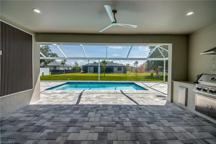 View of pool with glass enclosure, ceiling fan, exterior kitchen, a patio area, and a lawn