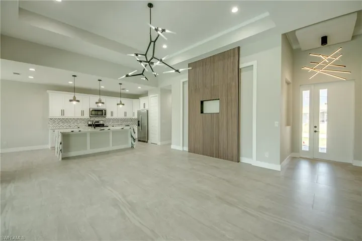 Unfurnished living room with a raised ceiling, french doors, light tile patterned floors, and a chandelier