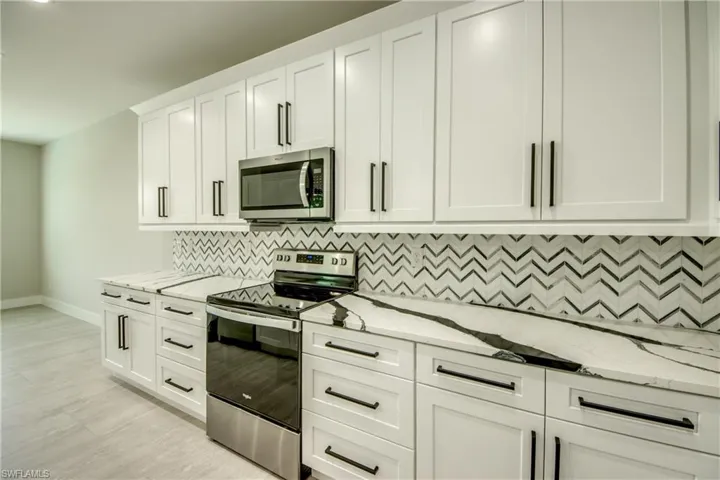 Kitchen featuring decorative backsplash, light stone counters, appliances with stainless steel finishes, white cabinets, and light hardwood / wood-style floors