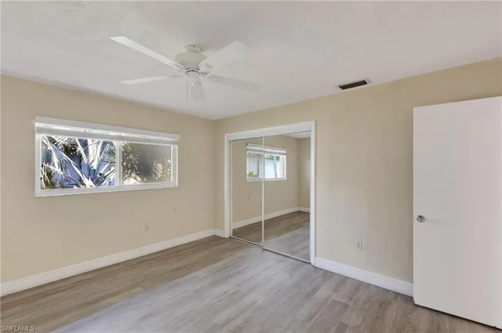 Room featuring wood-finish flooring, sliding mirrored closet doors, a white ceiling fan, and horizontal sliding windows