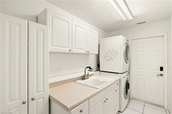 Laundry area featuring cabinets, sink, light tile patterned floors, and stacked washer and clothes dryer