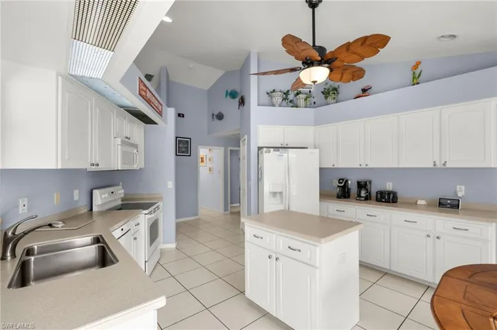 Kitchen featuring ceiling fan, a center island, sink, white appliances, and white cabinetry