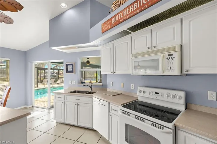 Kitchen featuring ceiling fan, sink, white appliances, white cabinetry, and light tile patterned flooring