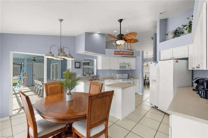Tiled dining area with high vaulted ceiling, plenty of natural light, sink, and ceiling fan with notable chandelier