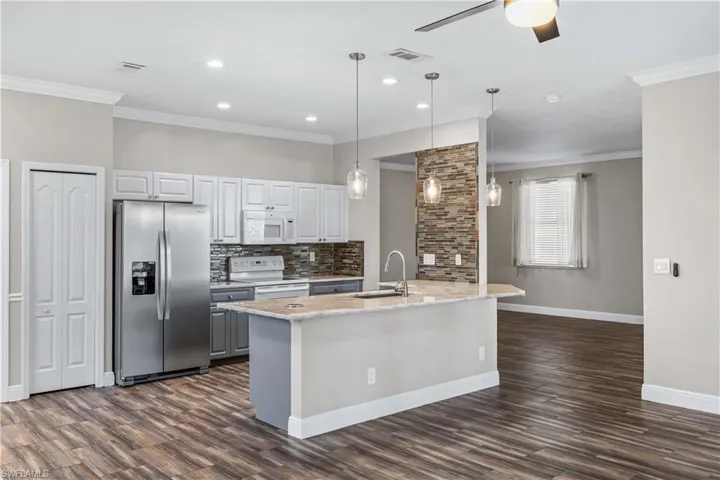 Kitchen with white appliances, hanging light fixtures, dark wood-style flooring, light stone countertops, and tasteful backsplash