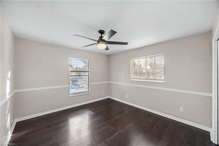 Unfurnished room featuring dark wood-type flooring, a ceiling fan, and plenty of natural light