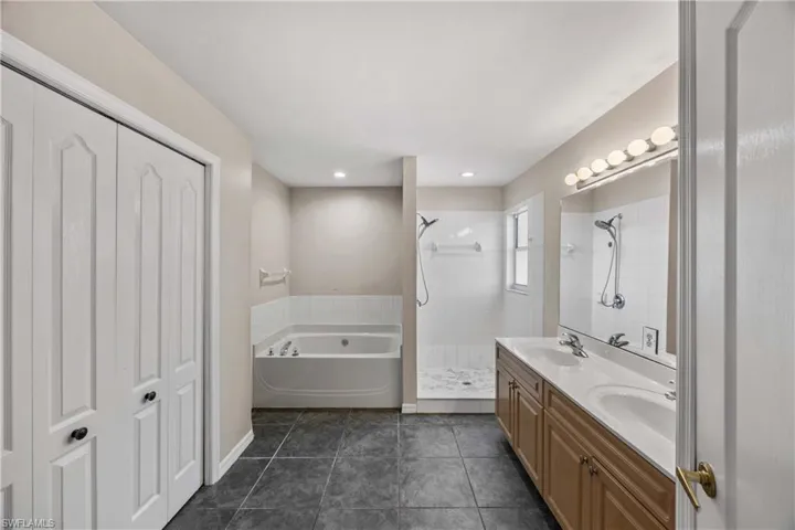 Full bathroom featuring a bath, double vanity, a tile shower, and dark tile patterned floors