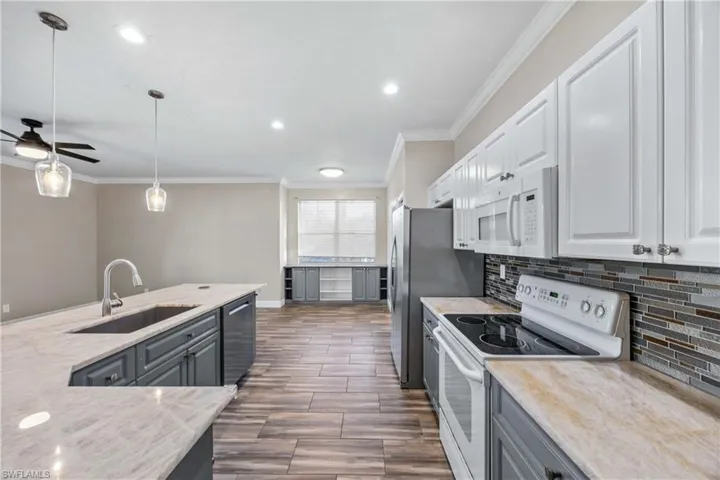 Kitchen featuring white appliances, ornamental molding, hanging light fixtures, a ceiling fan, and light stone counters