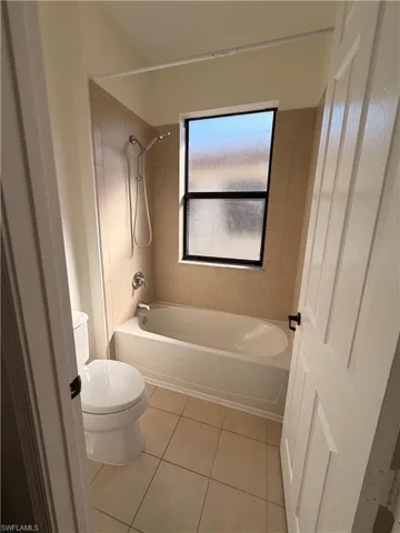 Full bathtub with integrated shower, chrome fixtures, and tiled surround