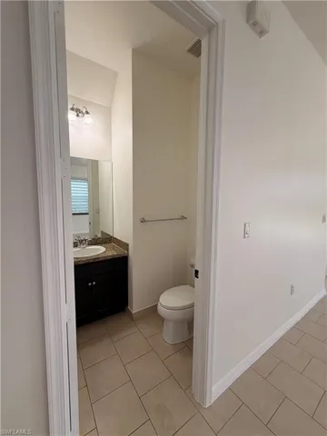 Tile flooring, dark wood-finish vanity, granite countertop, wall-mounted mirror, and white toilet