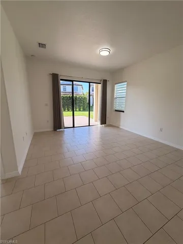 Neutral tone tile flooring, sliding glass patio doors, window with blinds, flush-mount ceiling light fixture