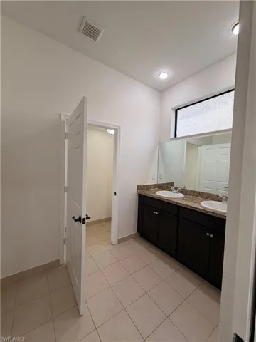 Dual vanity with under-mount sinks, granite countertop, dark wood-finish cabinetry, and tiled flooring
