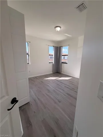 Neutral wall finishes, wood-finish flooring, two corner windows, and an overhead flush mount light fixture