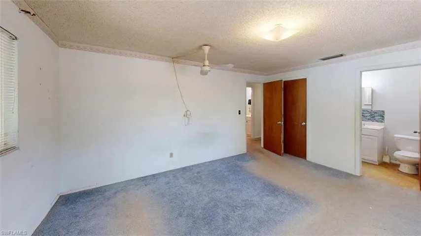 Unfurnished bedroom with carpet floors, a closet, a textured ceiling, and ensuite bath