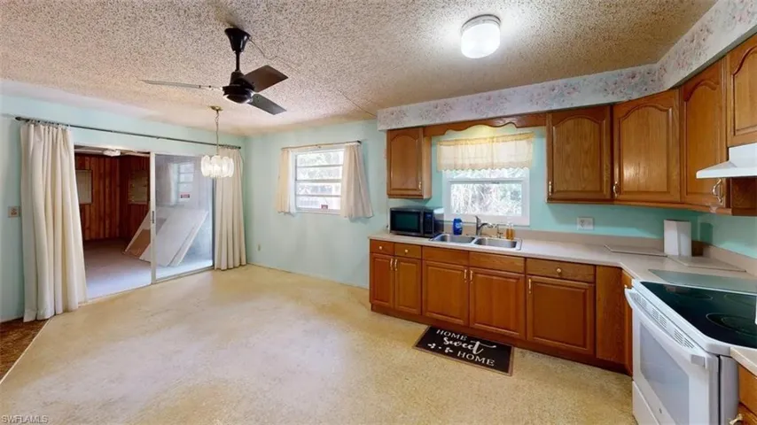 Kitchen featuring wood finish cabinetry, light countertops, a textured ceiling, electric stove, and ceiling fan