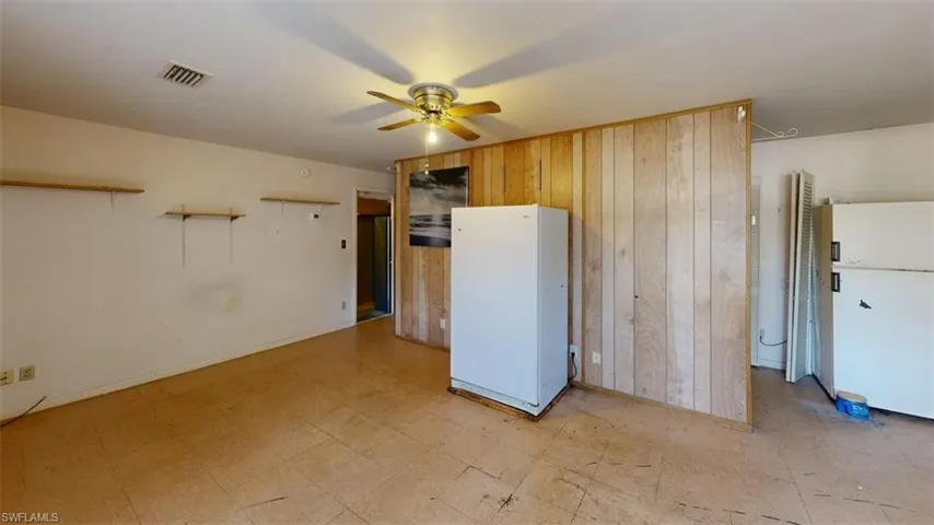 In-law suite featuring light floors, freestanding refrigerator, wood walls, and ceiling fan