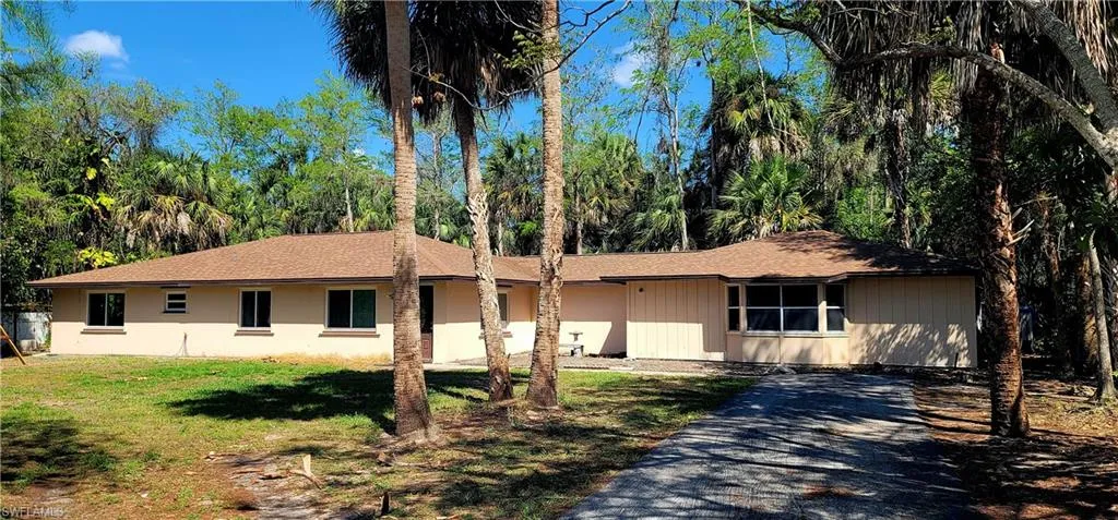 Ranch-style home featuring a front lawn, roof with shingles, and driveway