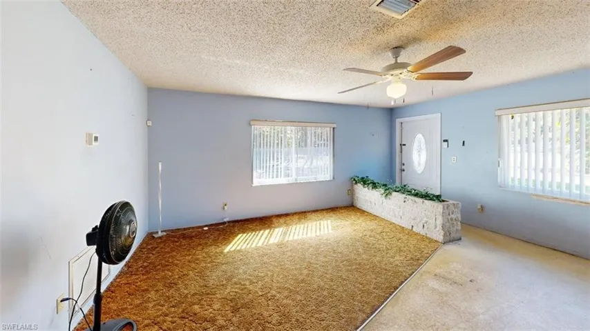 Unfurnished living room with a ceiling fan, plenty of natural light, a textured ceiling, and carpet flooring