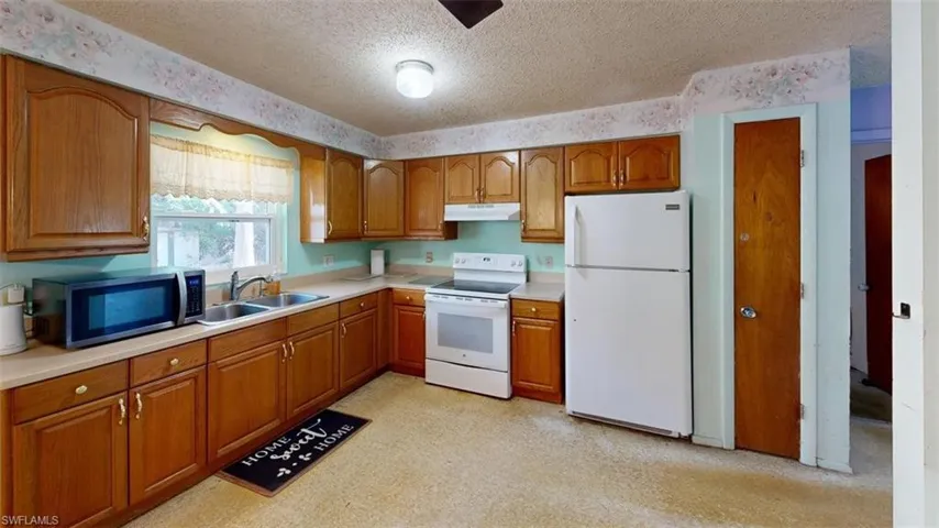 Kitchen featuring white appliances, wood finish cabinets, a textured ceiling, light countertops, and light floors