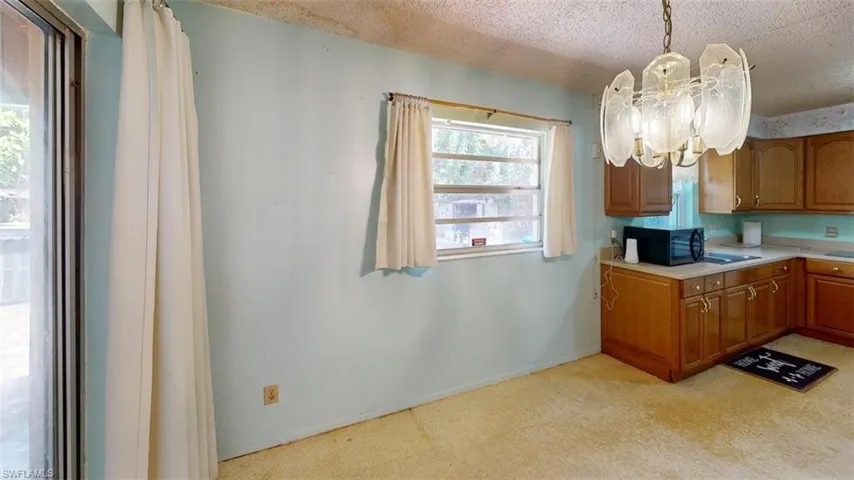 Kitchen featuring light countertops, wood finish cabinetry, suspended lighting, black microwave, and a textured ceiling