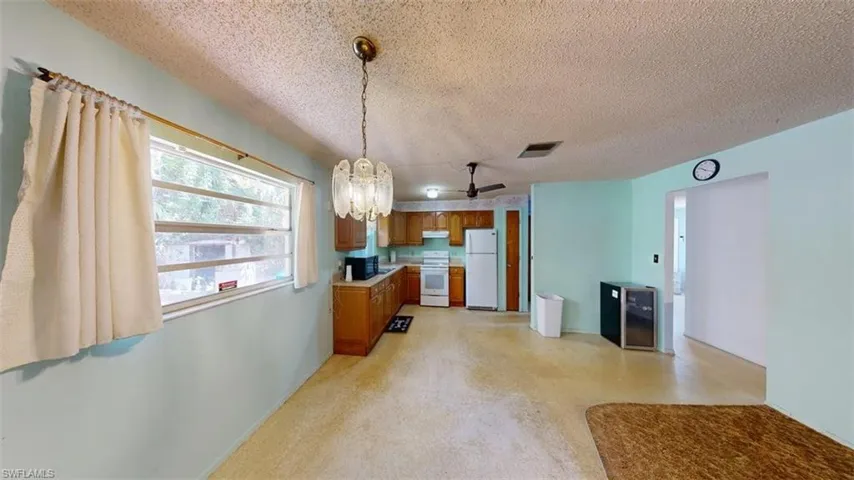 Kitchen with wood finish cabinetry, suspended lighting, a textured ceiling, light countertops, and white appliances