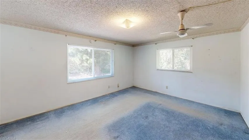 Carpeted empty room featuring a ceiling fan, plenty of natural light, and a textured ceiling