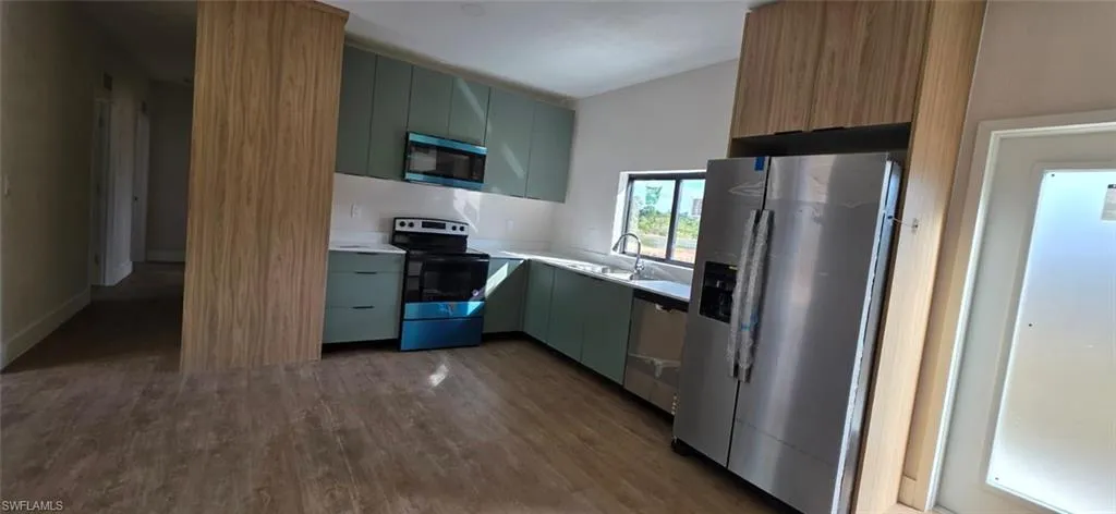 Kitchen with stainless steel appliances, light countertops, dark wood-style flooring, green cabinetry, and modern cabinets