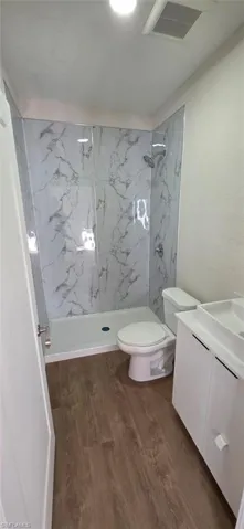Full bathroom with a marble finish shower, vanity, and dark wood-style floors