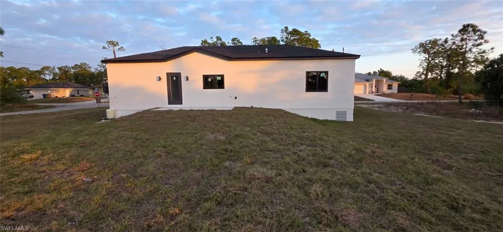 Back of property at dusk featuring a lawn, a patio area, and stucco siding