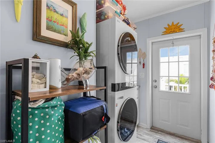 Laundry room with stacked washer / drying machine, ornamental molding, and light hardwood / wood-style flooring