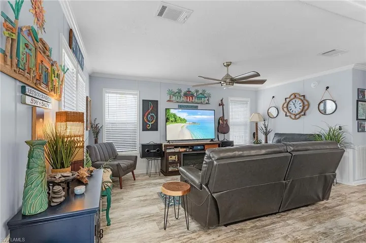 Living room with light wood-type flooring, crown molding, ceiling fan, and a healthy amount of sunlight