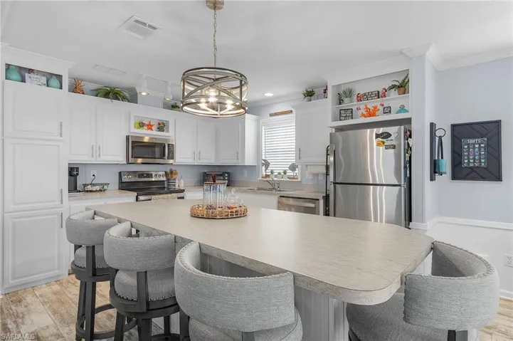 Kitchen featuring appliances with stainless steel finishes, ornamental molding, decorative light fixtures, light hardwood / wood-style flooring, and white cabinetry